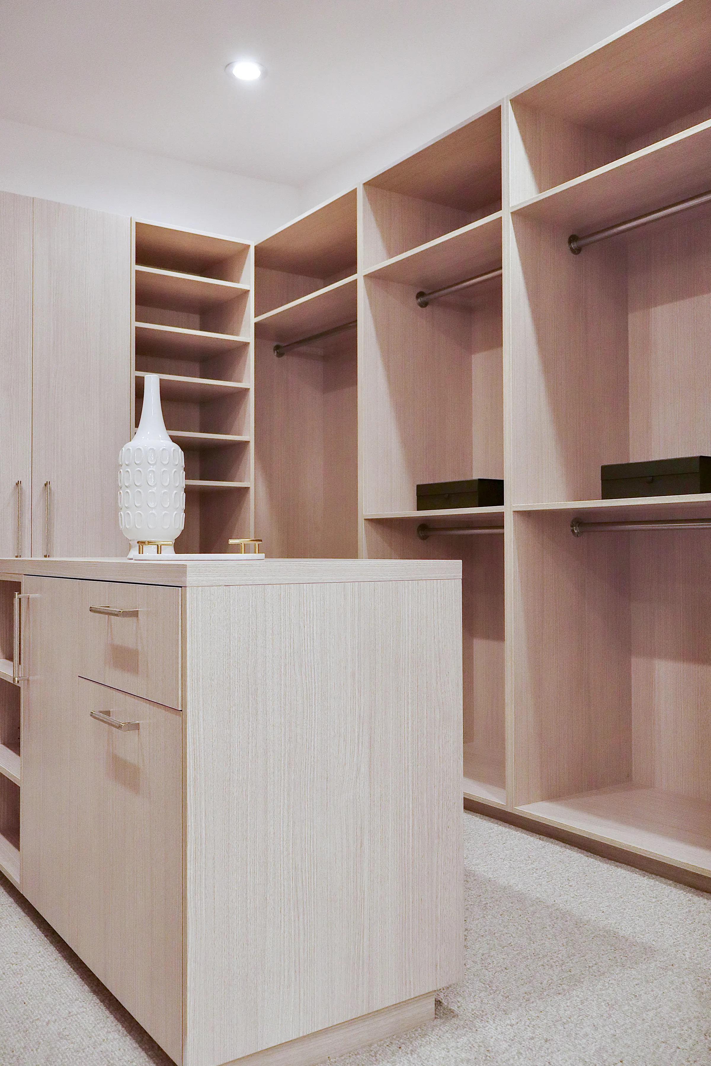 Pale oak closet island with drawers in front of double-height hanging sections