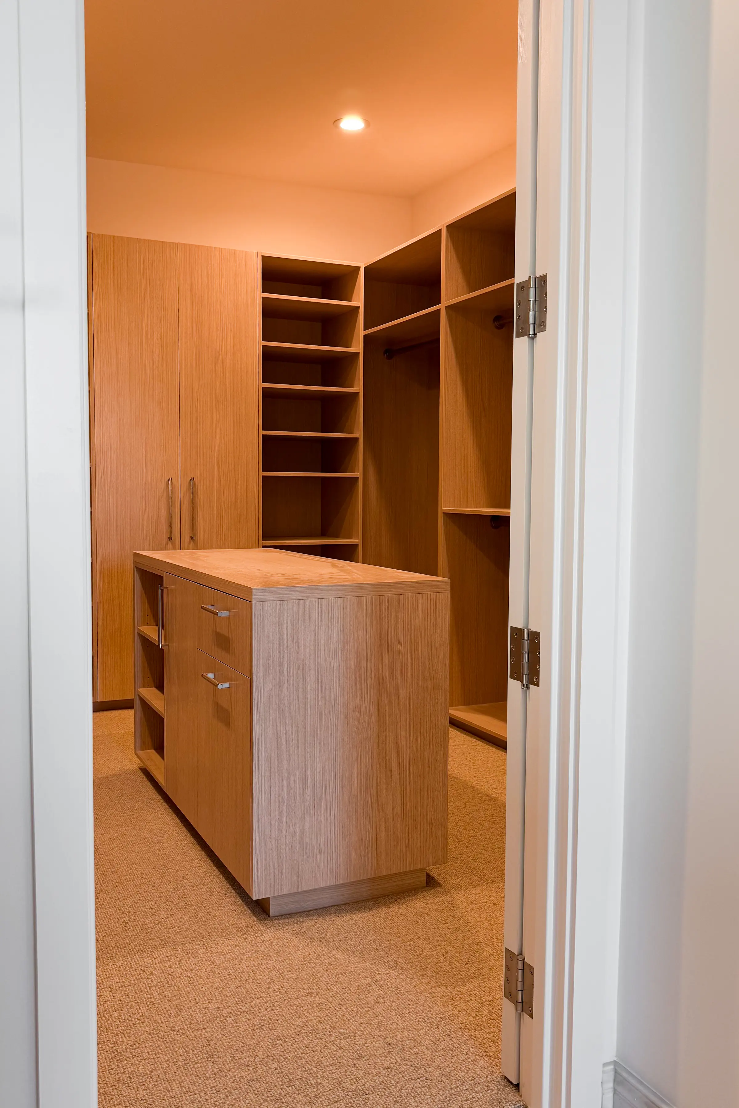 View through a doorway into a walk-in closet with an oak island, wardrobe doors and hanging sections
