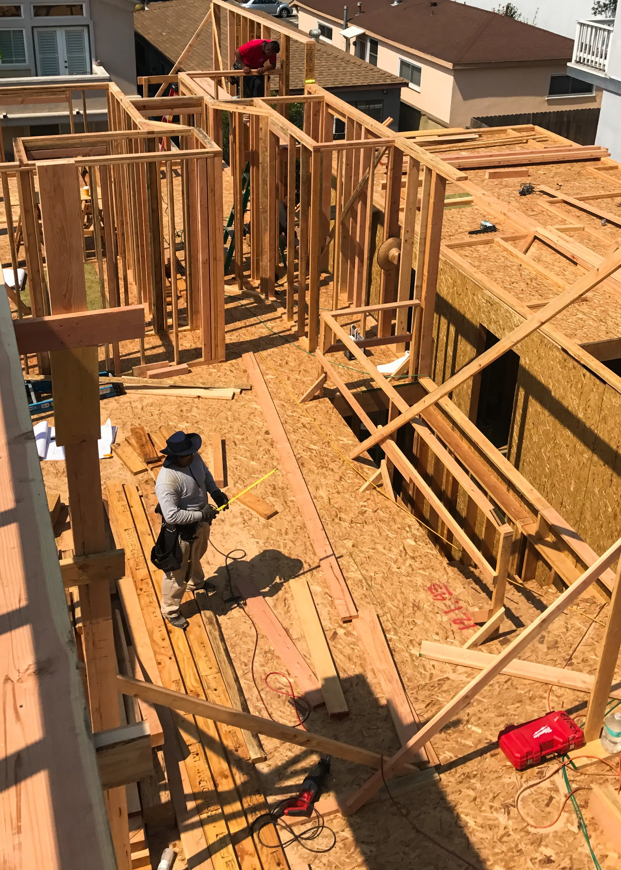 Second-floor wall framing on a new residence, seen from above, with a carpenter measuring lumber