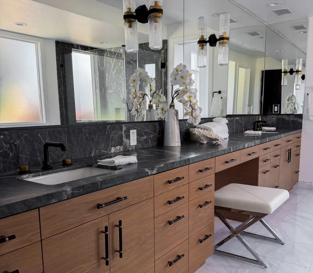 The same primary bathroom after the remodel: dark marble counters and backsplash, rift-cut oak vanity, black fixtures and fluted glass sconces