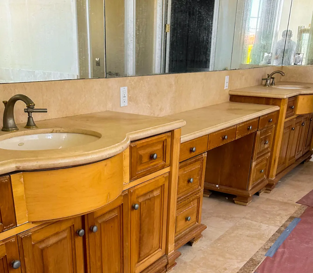 Primary bathroom before the remodel: honey-toned wood vanities, curved travertine counters and brass fixtures