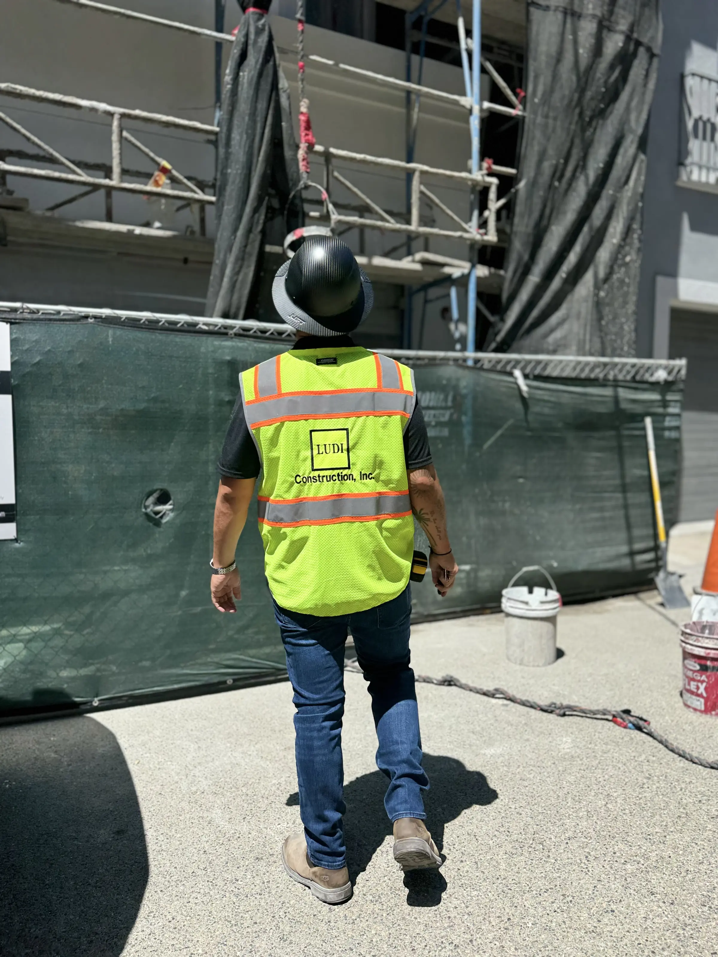 Ludi Construction team member in a branded vest and hard hat beside a scaffolded façade
