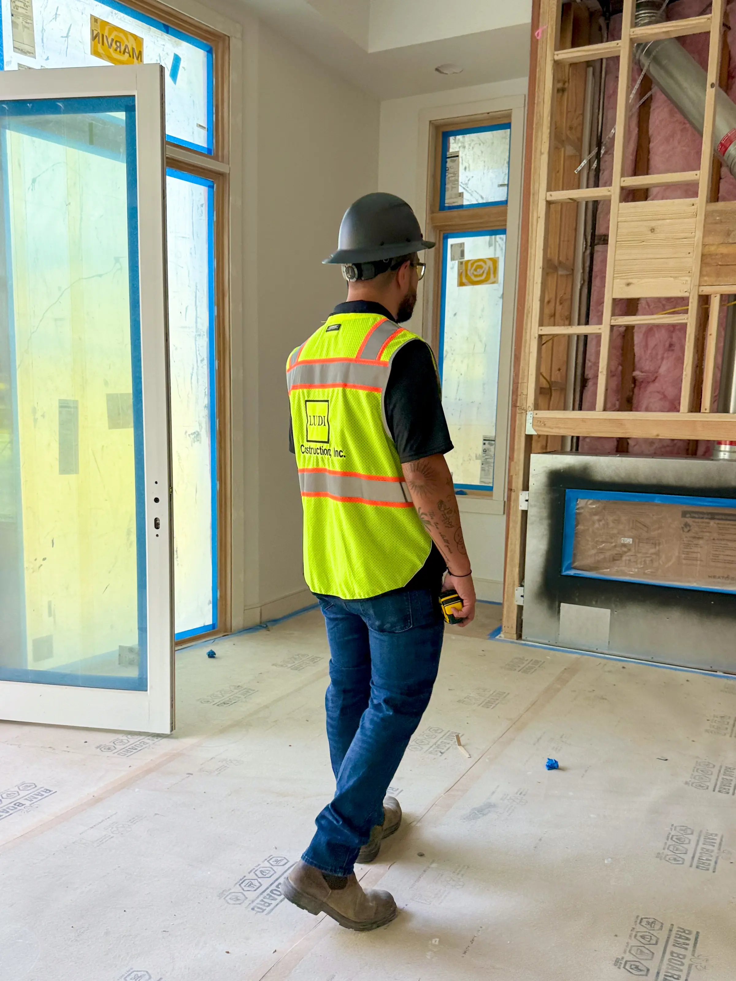 Ludi Construction team member in a branded safety vest walking a room with new windows and open framing