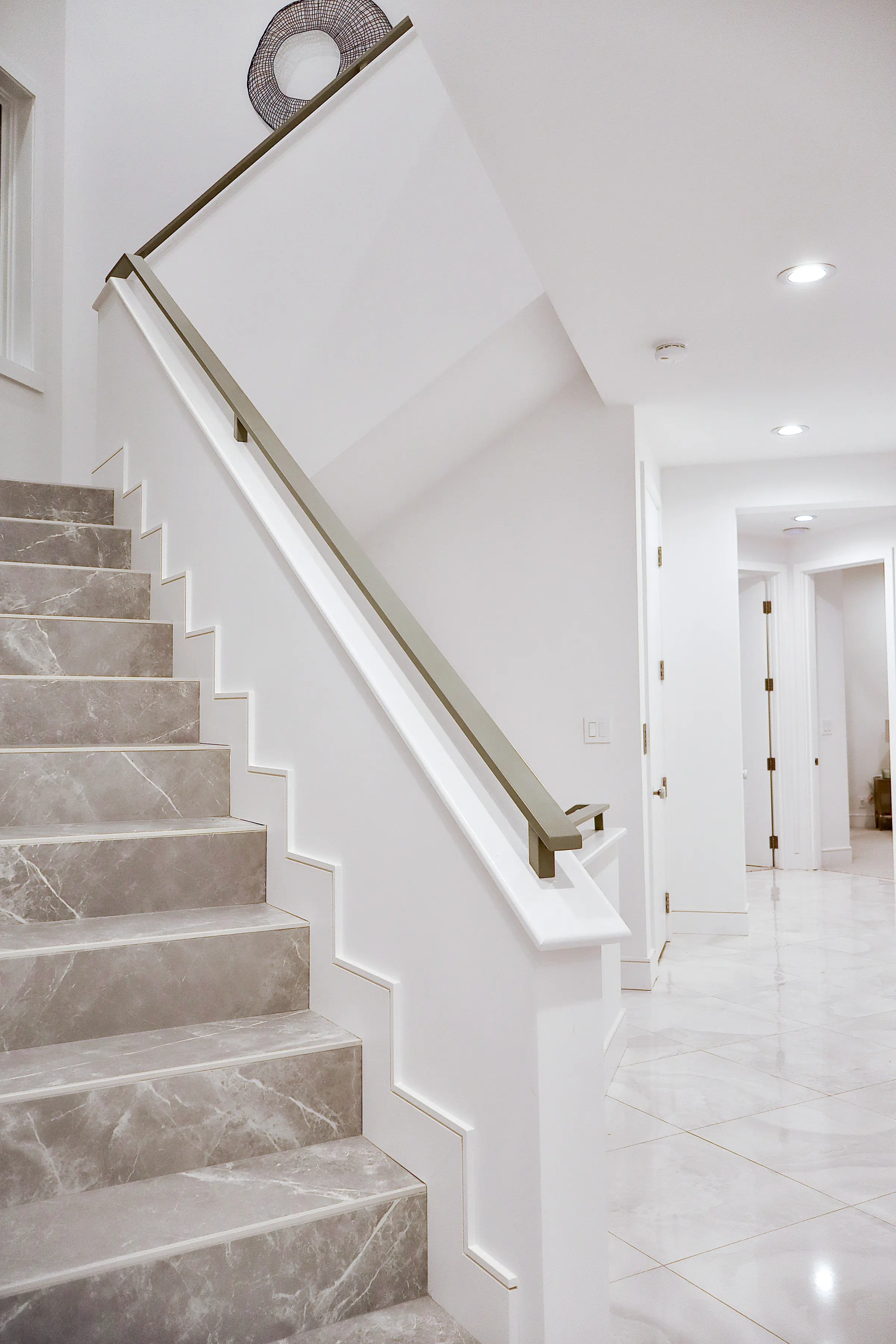 Grey marble stair with white stepped skirting and a slim bronze-finish handrail, leading to a white marble hall