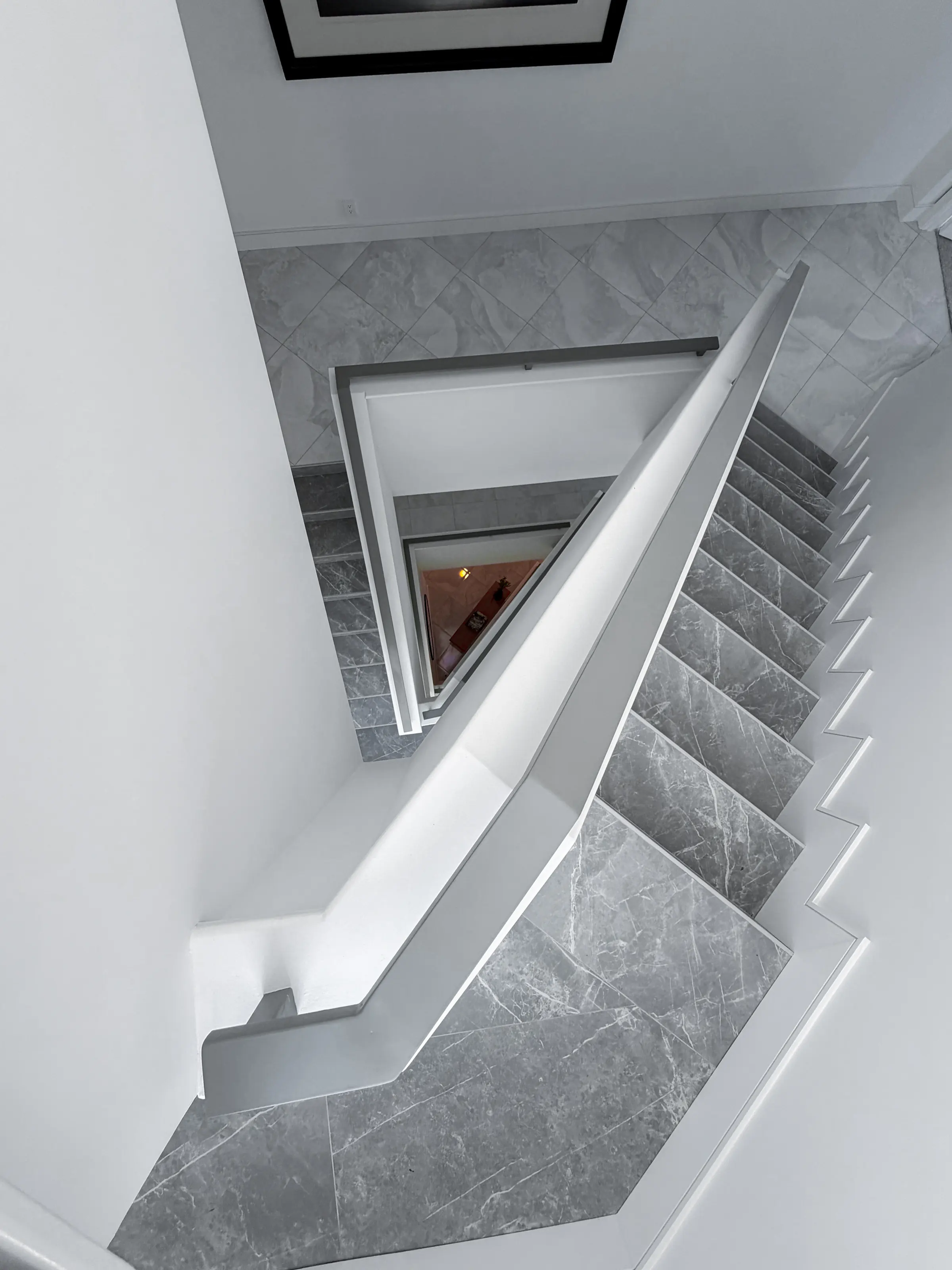 Stairwell seen from above: grey veined marble treads wrapping around a white plaster guard wall